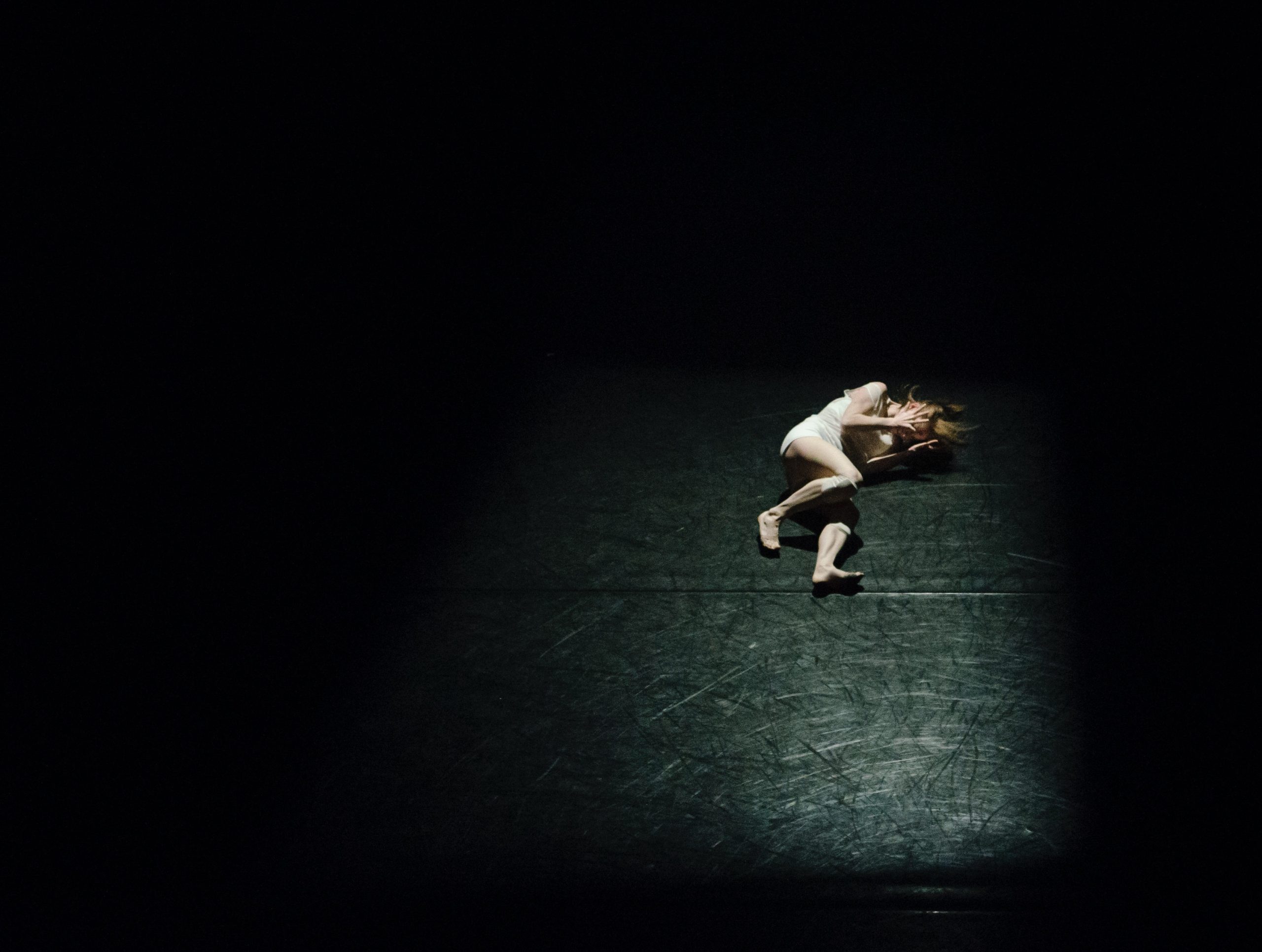 Photo of a female lying down on the ground with her hands to her head in discomfort.