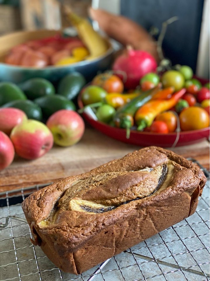 loaf of banana bread cooling on a wire rack with fresh fruit in the background