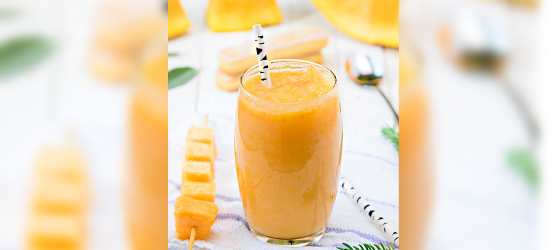 mango smoothie in a glass with straw, and mango cubes on a skewer beside.